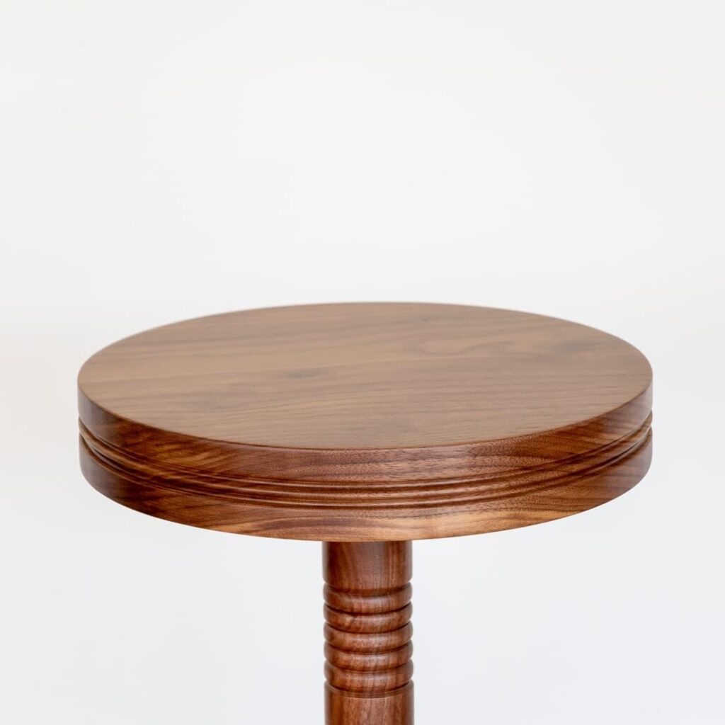 This elegant and versatile wooden drink table is a beautiful addition to any home or commercial space. The circular tabletop is crafted from high-quality walnut wood, showcasing its natural grain and warm tones. The unique, intricately carved ribbed detailing on the central support adds a touch of artistry and visual interest. This table is perfect for serving drinks, snacks, or displaying decorative items