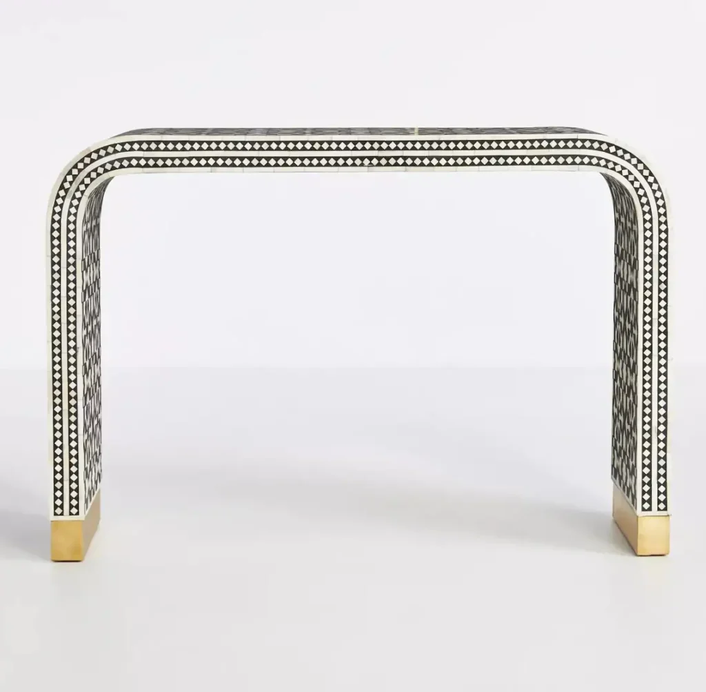 Bring a touch of elegance and craftsmanship to your living space with this exquisite Bone Inlay Console Table. Handcrafted by skilled artisans, this piece features intricate hand-carved bone details and curvaceous corners that create a sophisticated and timeless design. The console is made from solid wood and MDF for durability and longevity. Its base is accentuated with a brass cladding, offering a luxurious touch while enhancing the overall aesthetics. With its sleek and modern form, this console table is perfect for your entryway, living room, or hallway, adding both beauty and functionality to any space